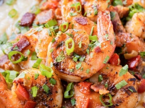 Seared blackened Gulf shrimp are served on top of creamy and cheesy grits in a black bowl.