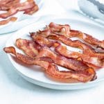 Bacon is placed on a white plate on the counter.