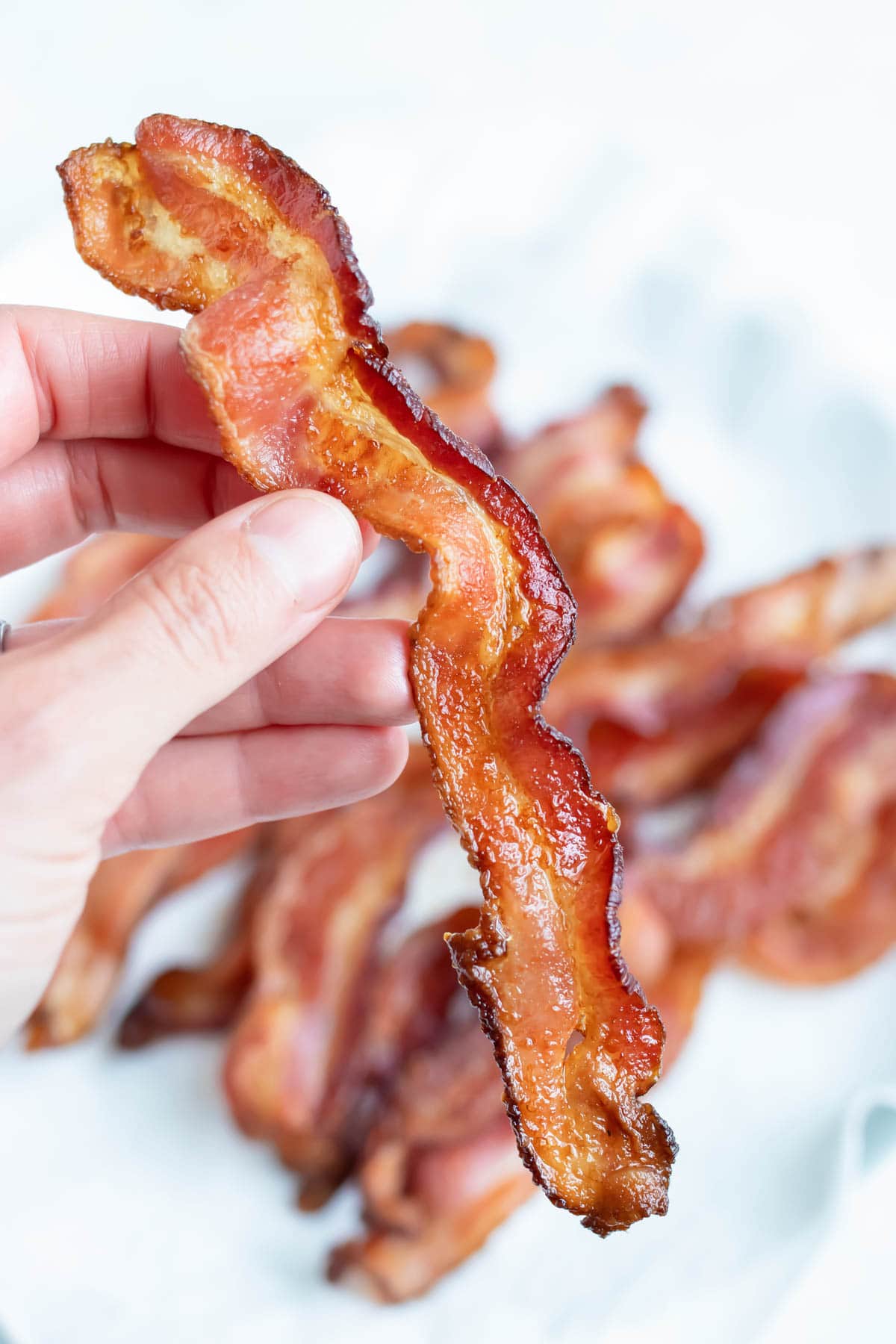 A hand lifts up slice of a slice of air fryer bacon.