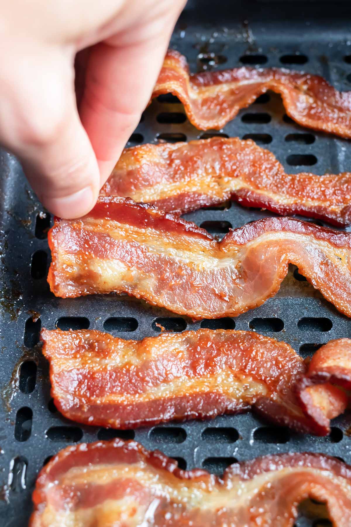 A slice of bacon is taken out of the air fryer after cooking.
