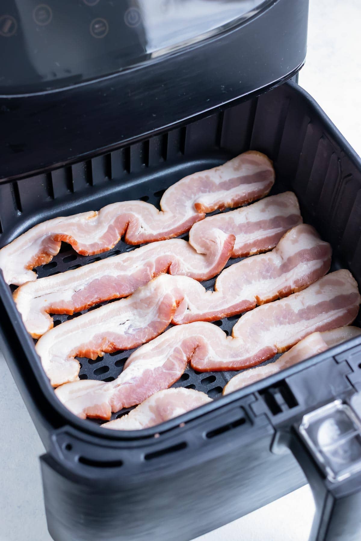 Slices of bacon are shown in the air fryer before cooking.