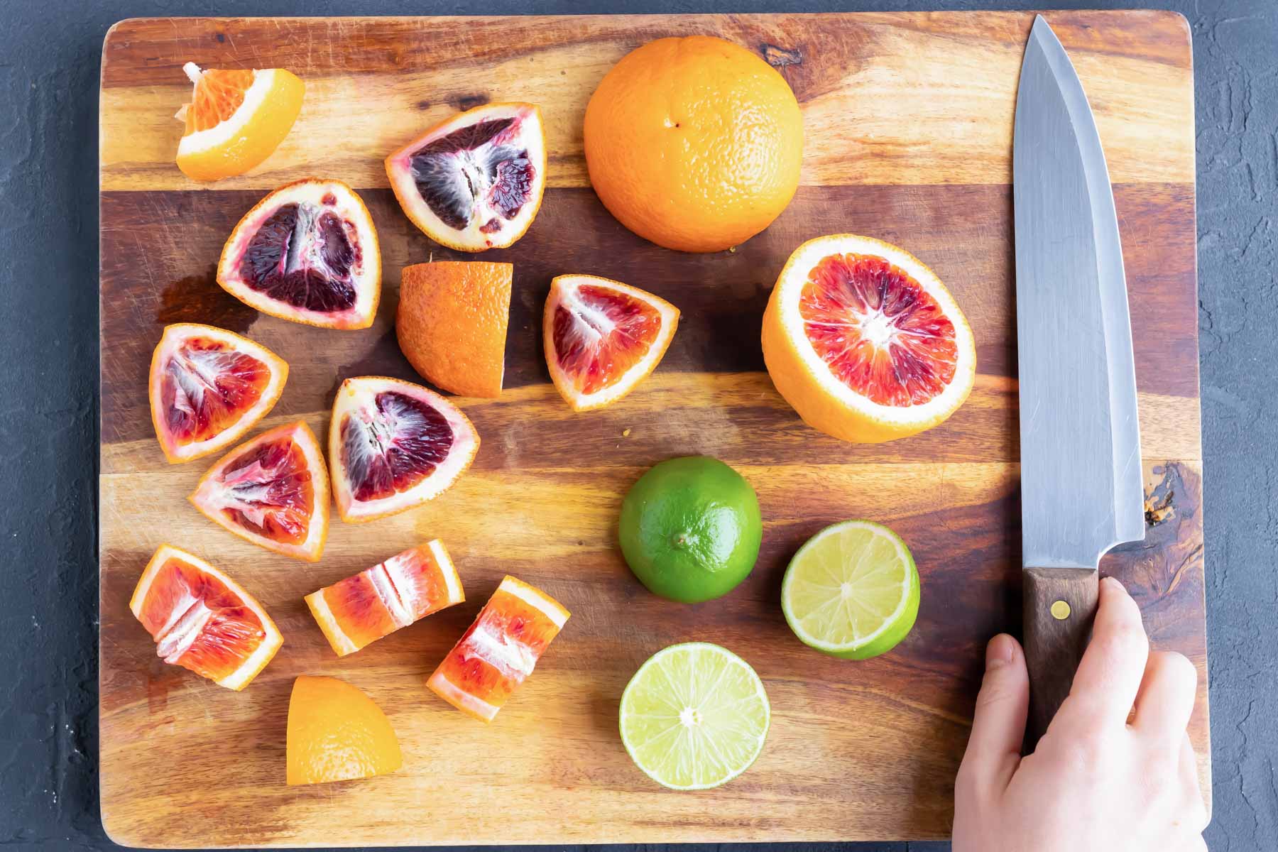 Blood oranges and limes being cut on a wooden cutting board.