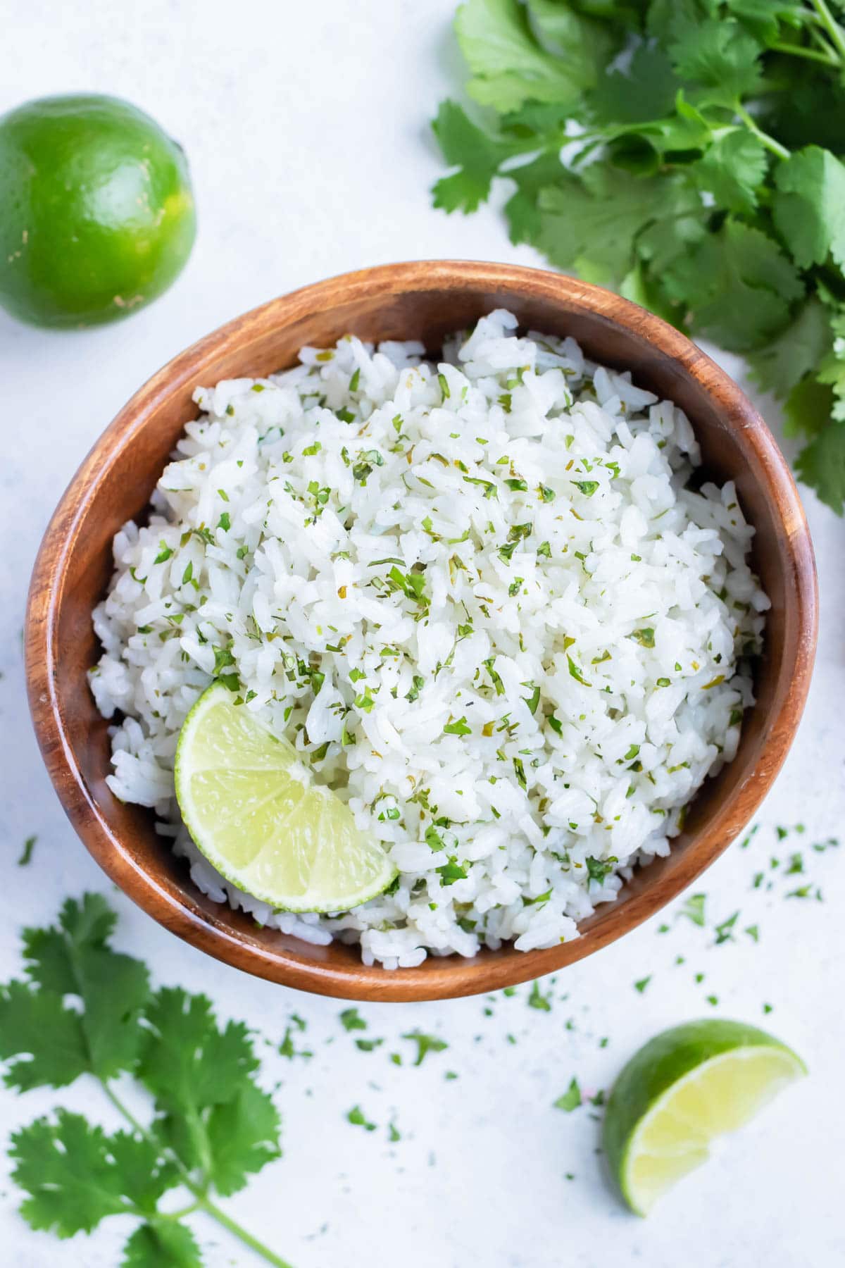 Cilantro Rice is served from a wooden bowl with fresh limes and cilantro.