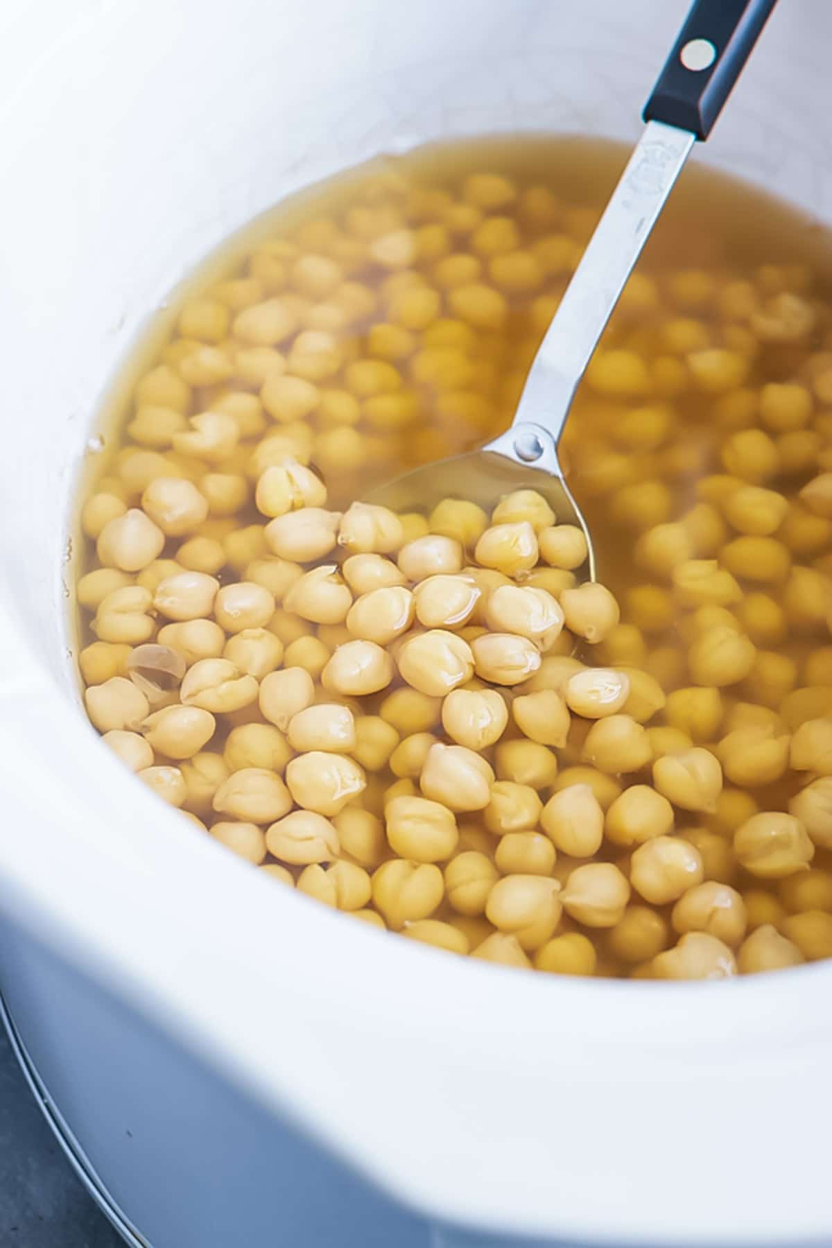 A spoon scooping out cooked garbanzo beans and showing how to cook chickpeas in the Crock-Pot.