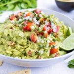A bowl full of an easy guacamole recipe with tomatoes and cilantro on top.