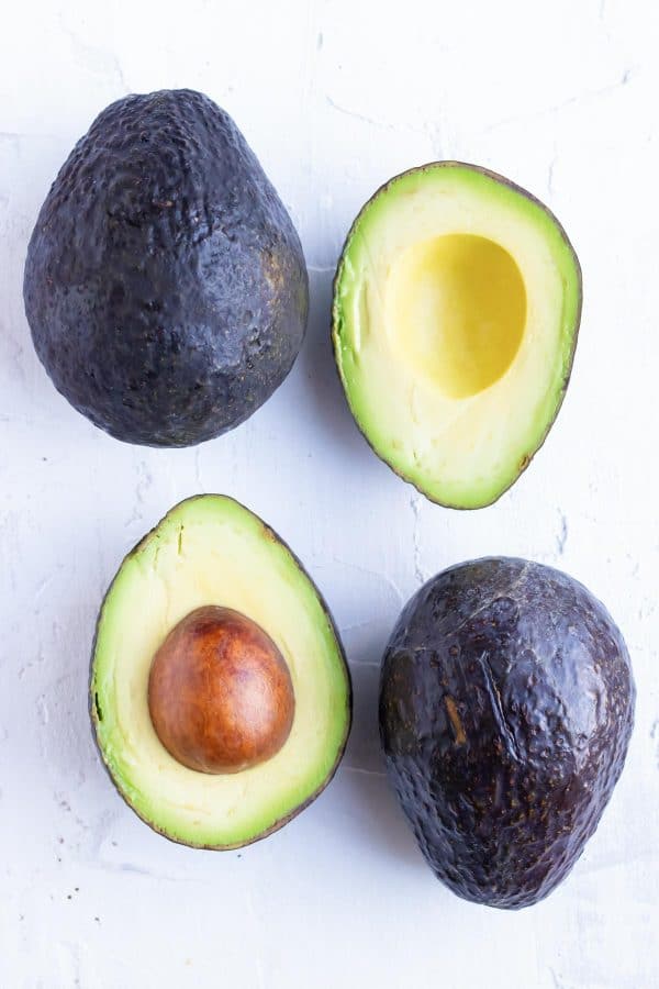 Two whole avocados and two avocado halves to show how to ripen avocados.