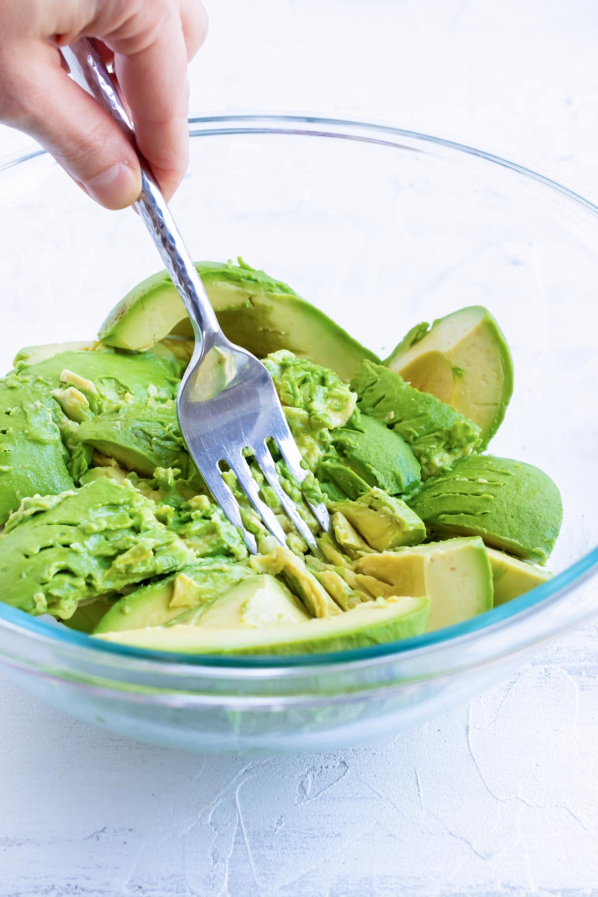 A fork mashes sliced avocados in a bowl.