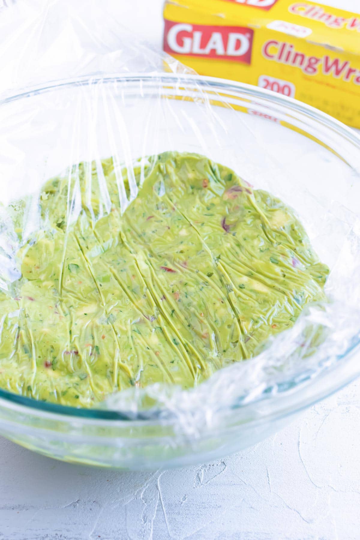 Homemade guacamole in a glass bowl with saran wrap on top to keep it from turning brown.