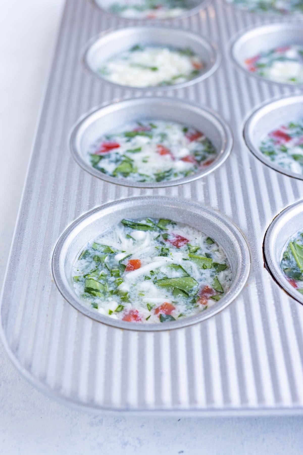 Egg white bite mixture and add-ins are poured into a muffin tray.