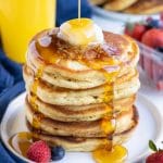 Syrup is poured over a stack of pancakes.