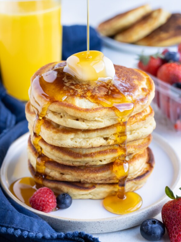 Syrup is poured over a stack of pancakes.
