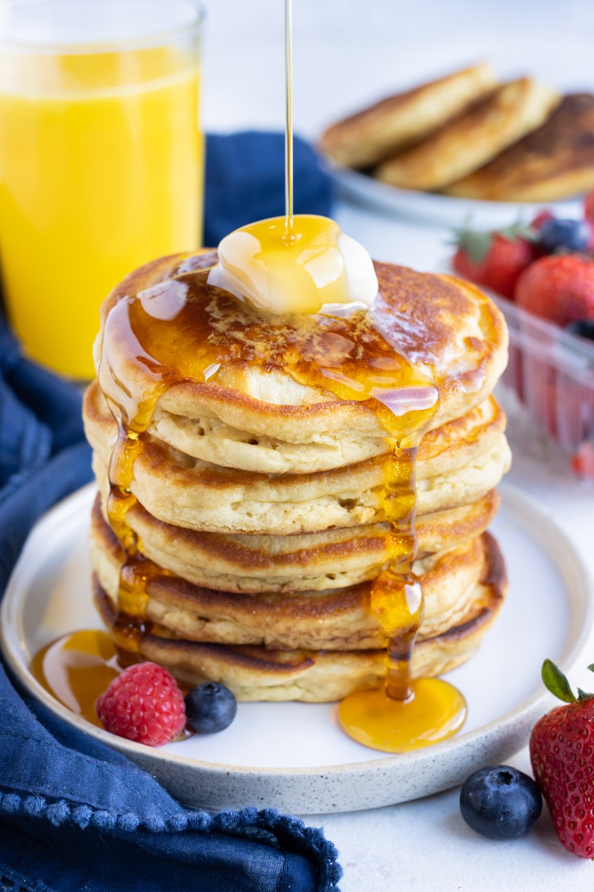 Syrup is poured over a stack of pancakes.