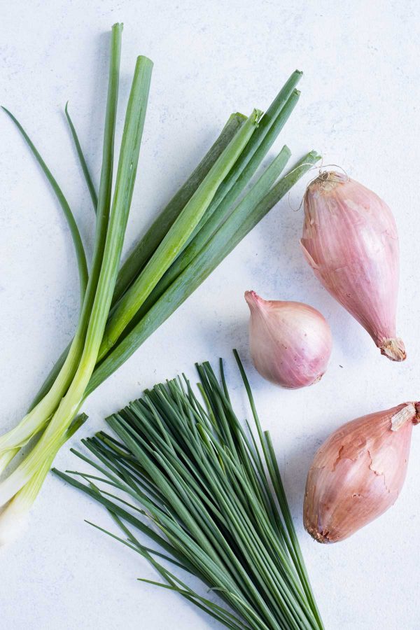 Green onions, chives, and shallots are set on the counter beside each other.