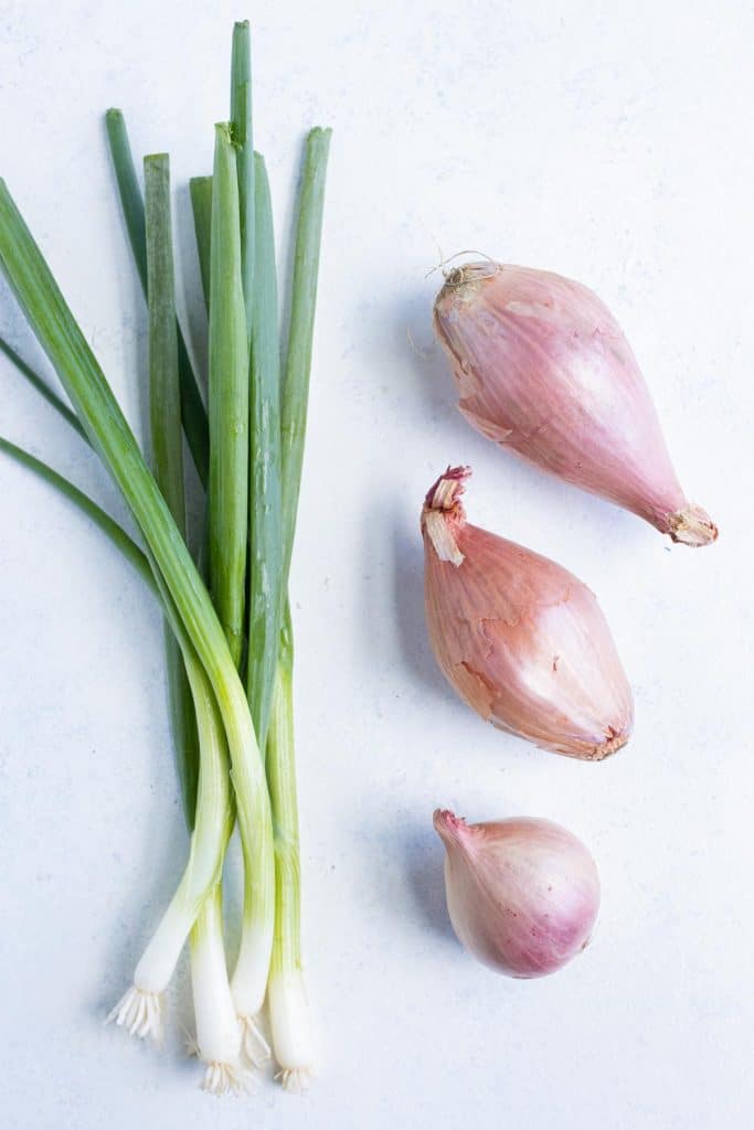 Three shallots are shown beside green onions on the counter.