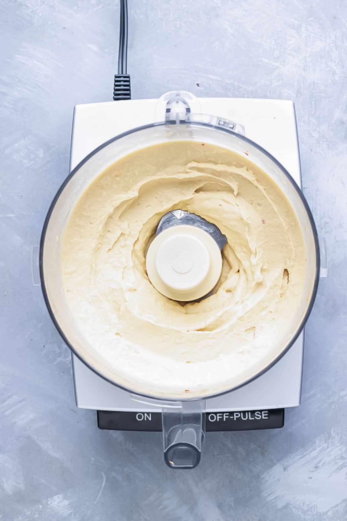 Fully blended hummus sits inside a food processor.