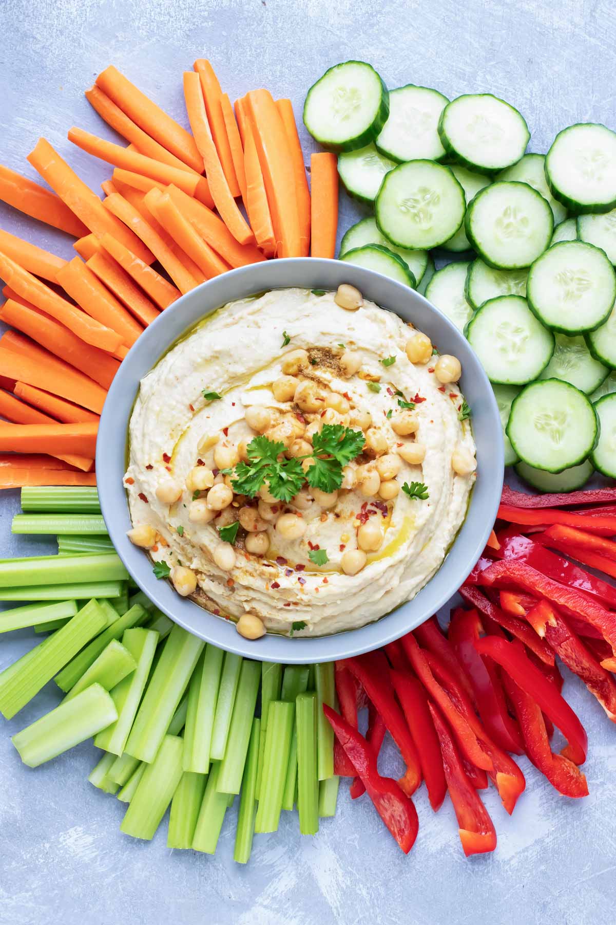 An easy hummus recipe in a grey bowl with carrots, cucumbers, bell peppers, and celery to serve with it.