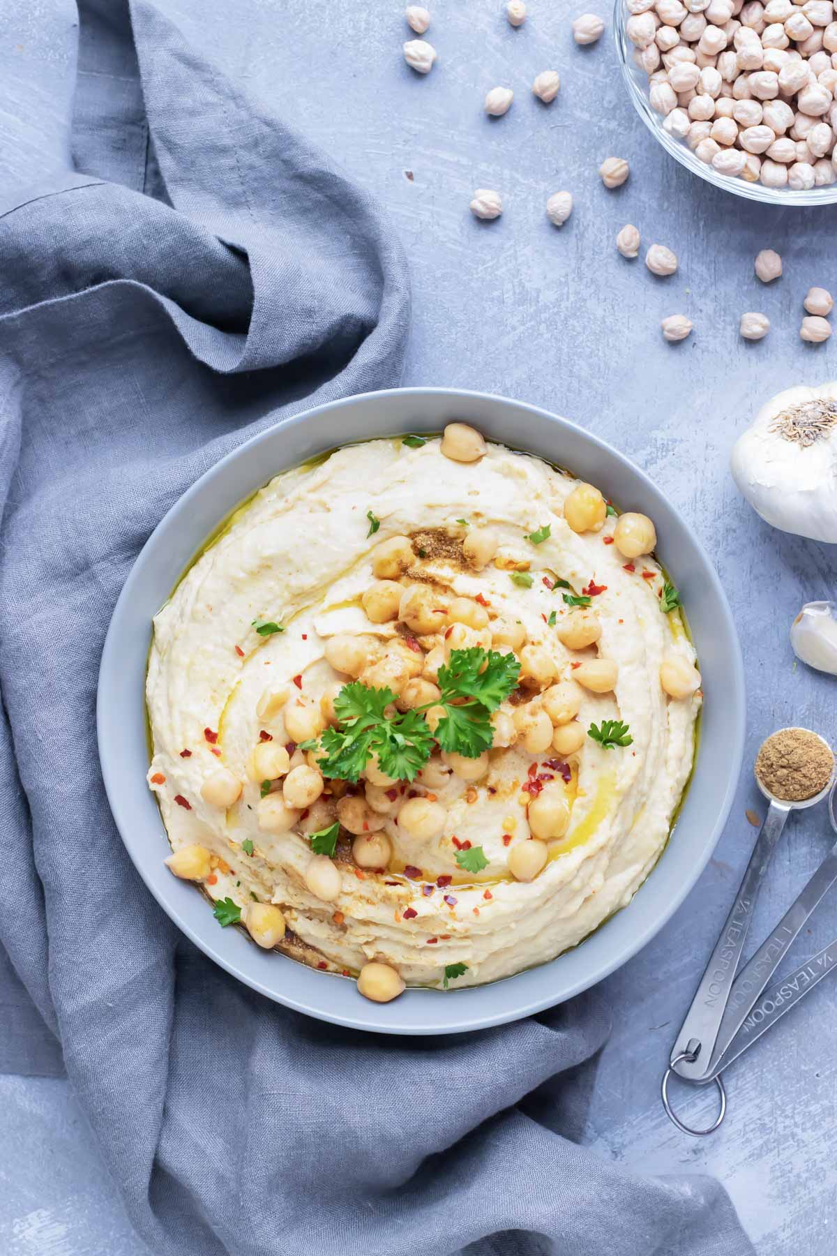Creamy, healthy, hummus in a silver bowl next to garlic and dried chickpeas.