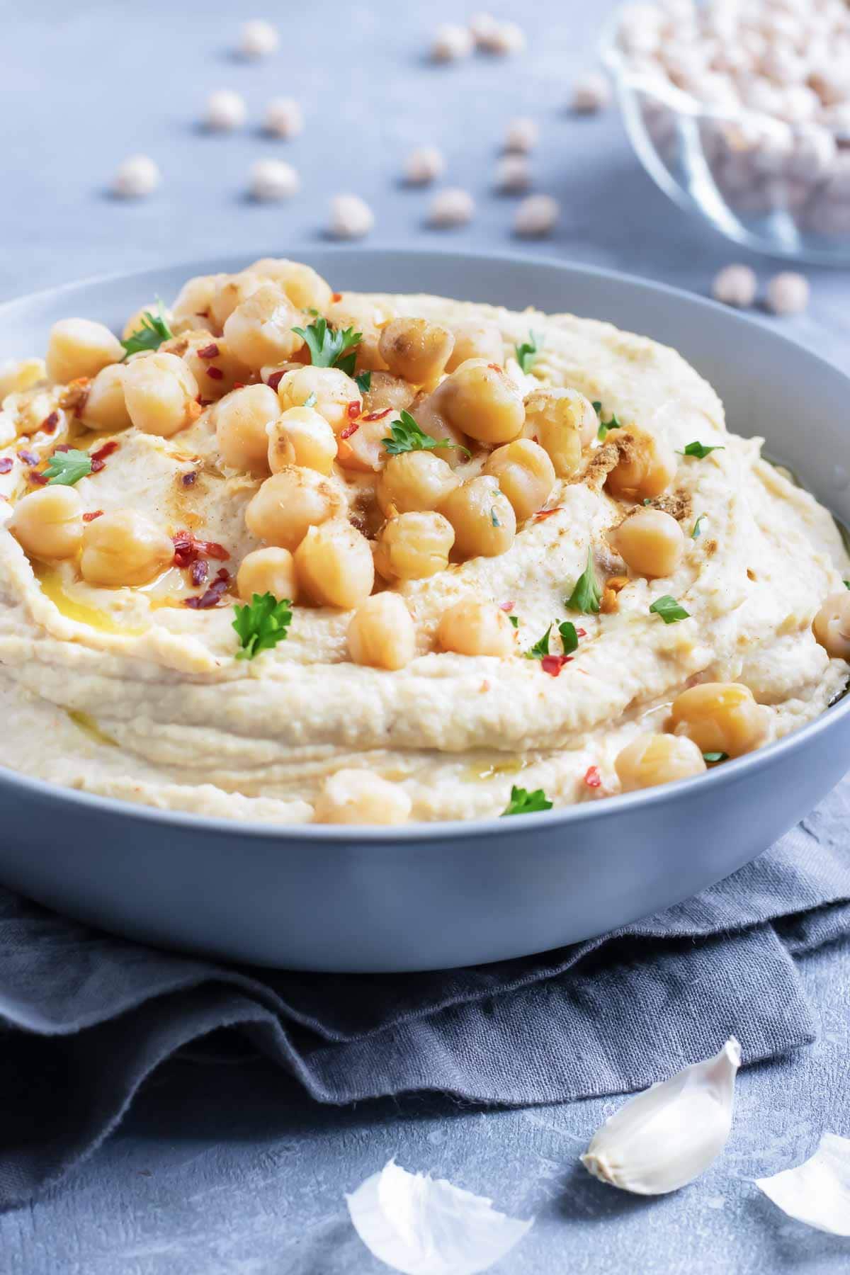 A bowl full of authentic hummus with chickpeas and parsley sprinkled on top.