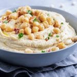A bowl full of the best hummus with chickpeas and parsley sprinkled on top.
