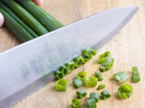 A sharp butcher's knife is used to finely chop the green onions.