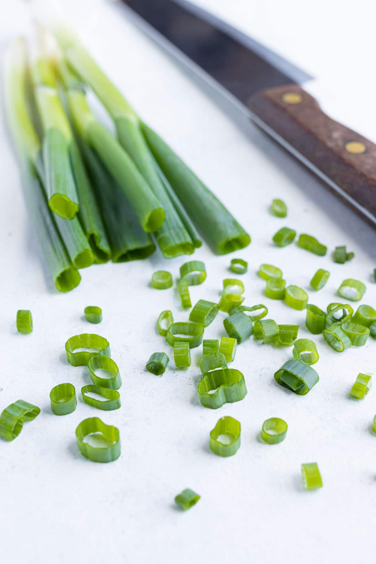 Chopped green onions are set on the counter near near whole green onions.