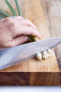 A knife is used to remove the stem from the green onions.