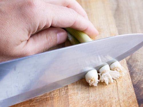 A knife is used to remove the stem from the green onions.