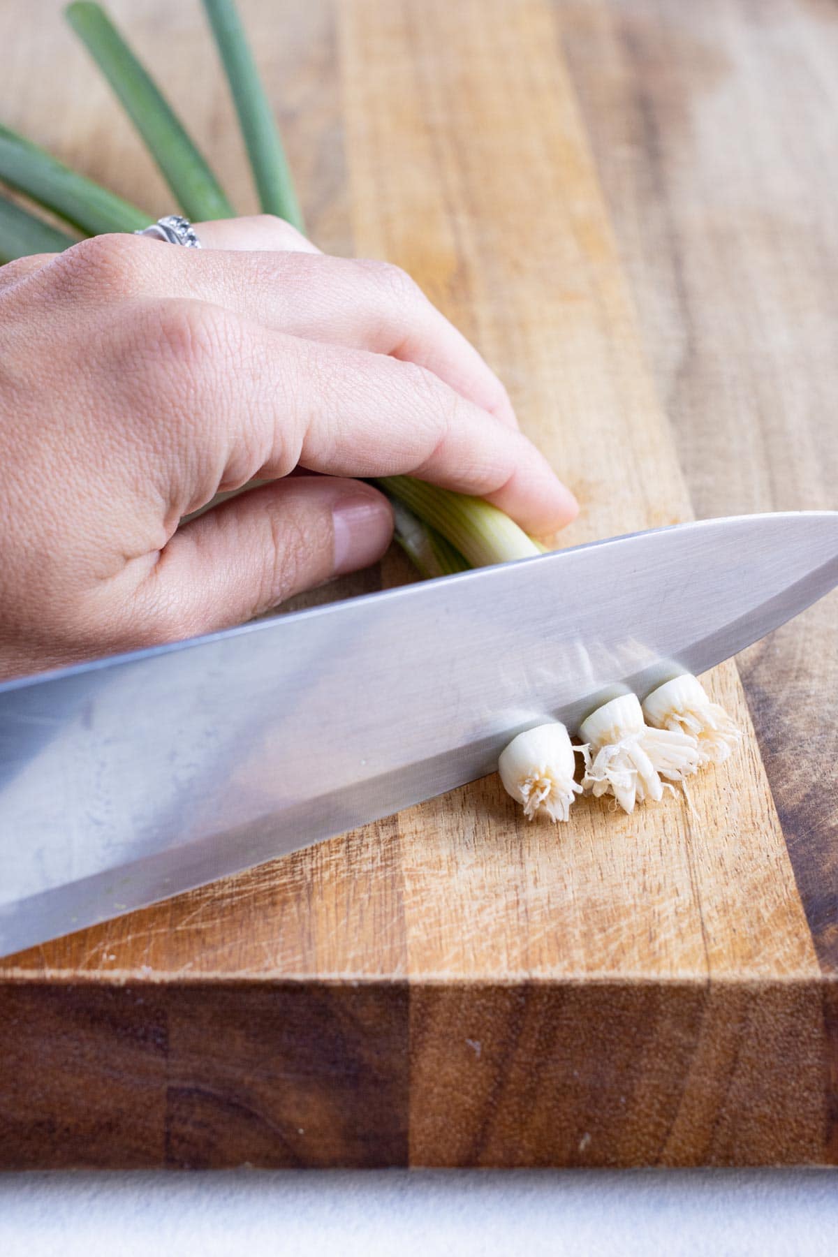 A knife is used to remove the stem from the green onions.