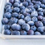 A layer of frozen blueberries is shown on the baking sheet.