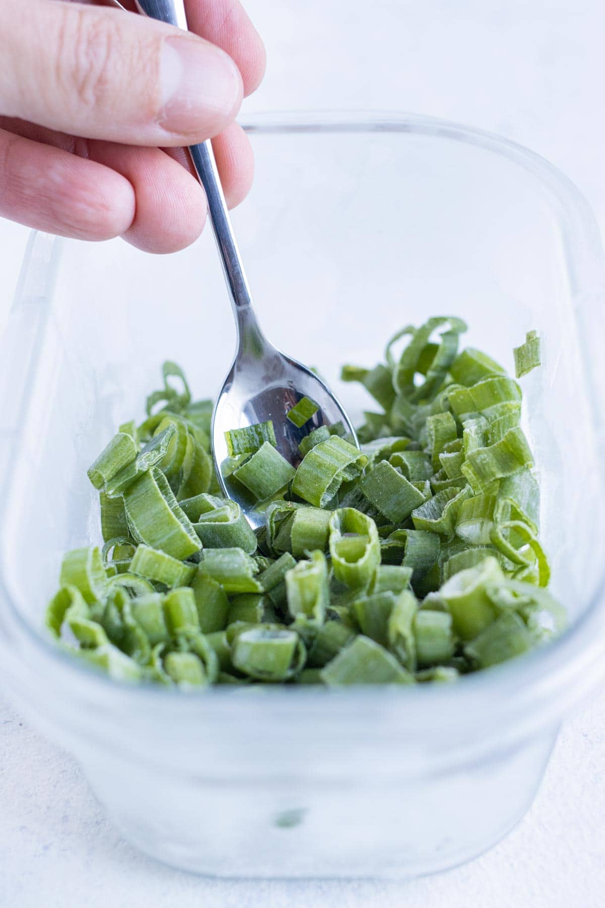 Green onions are tossed by a spoon.