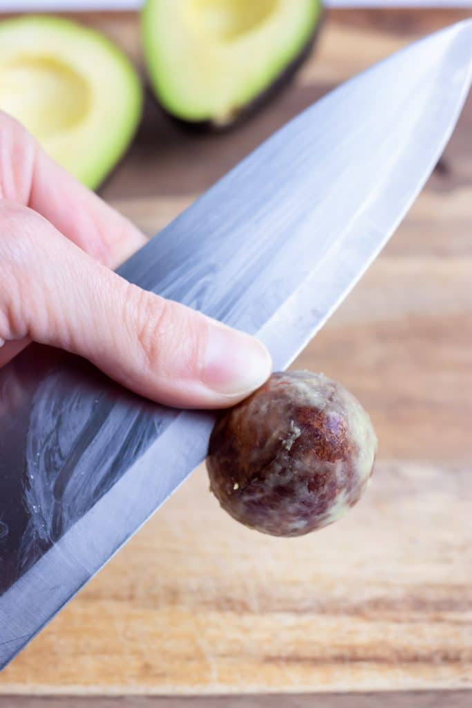 Fingers gently remove an avocado pit from a chef's knife.