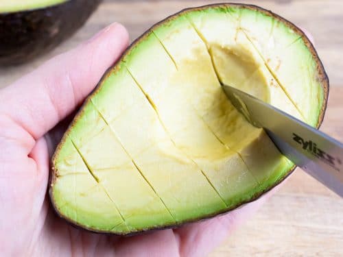 A halved avocado is cut into cubes.
