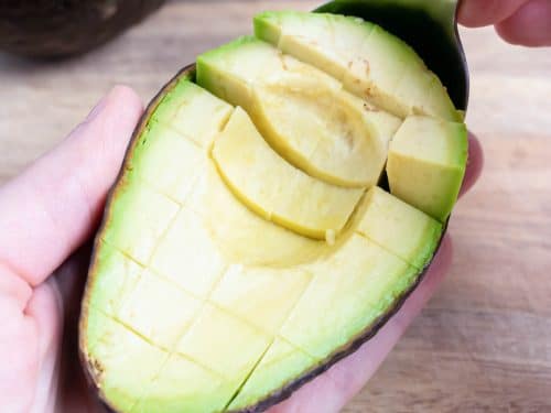 A spoon scoops cubed avocado out of its skin.