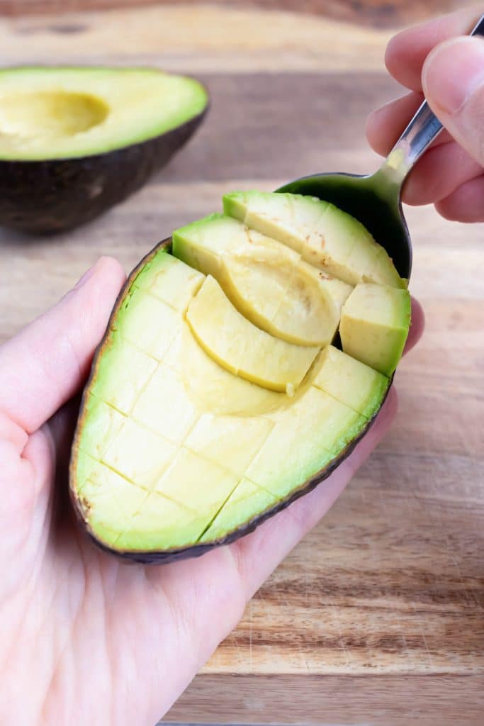 A spoon scoops cubed avocado out of its skin.