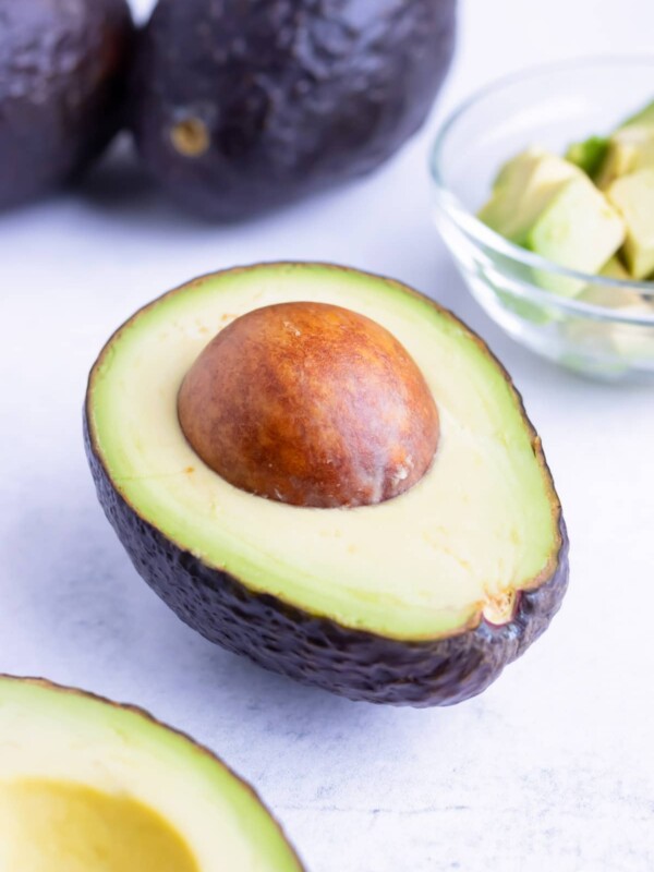 A cut avocado halve with the pit and cubes of avocado in the background.