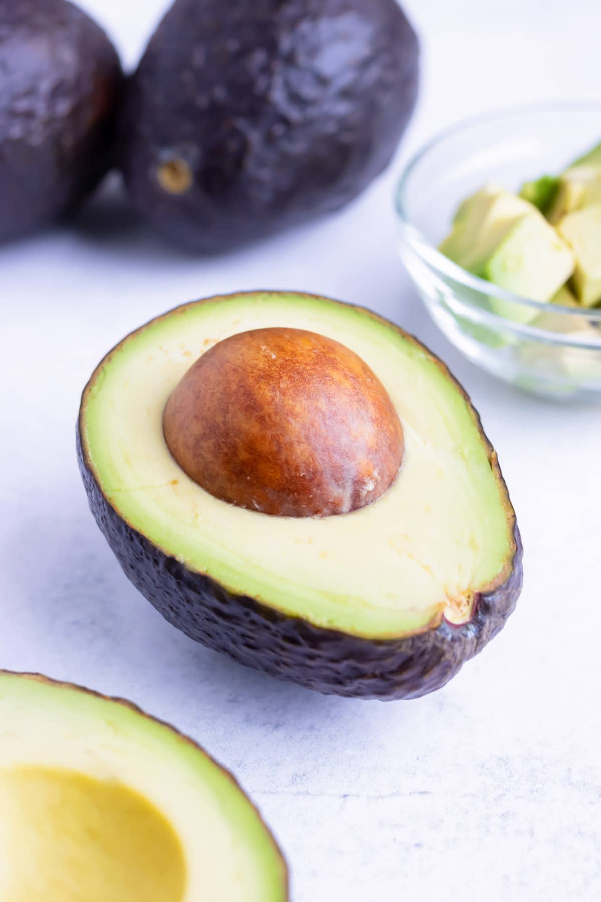 A cut avocado halve with the pit and cubes of avocado in the background.