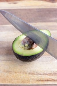 A knife is struck down into the pit of an avocado to remove it.