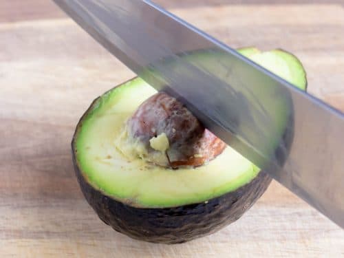 A knife is struck down into the pit of an avocado to remove it.