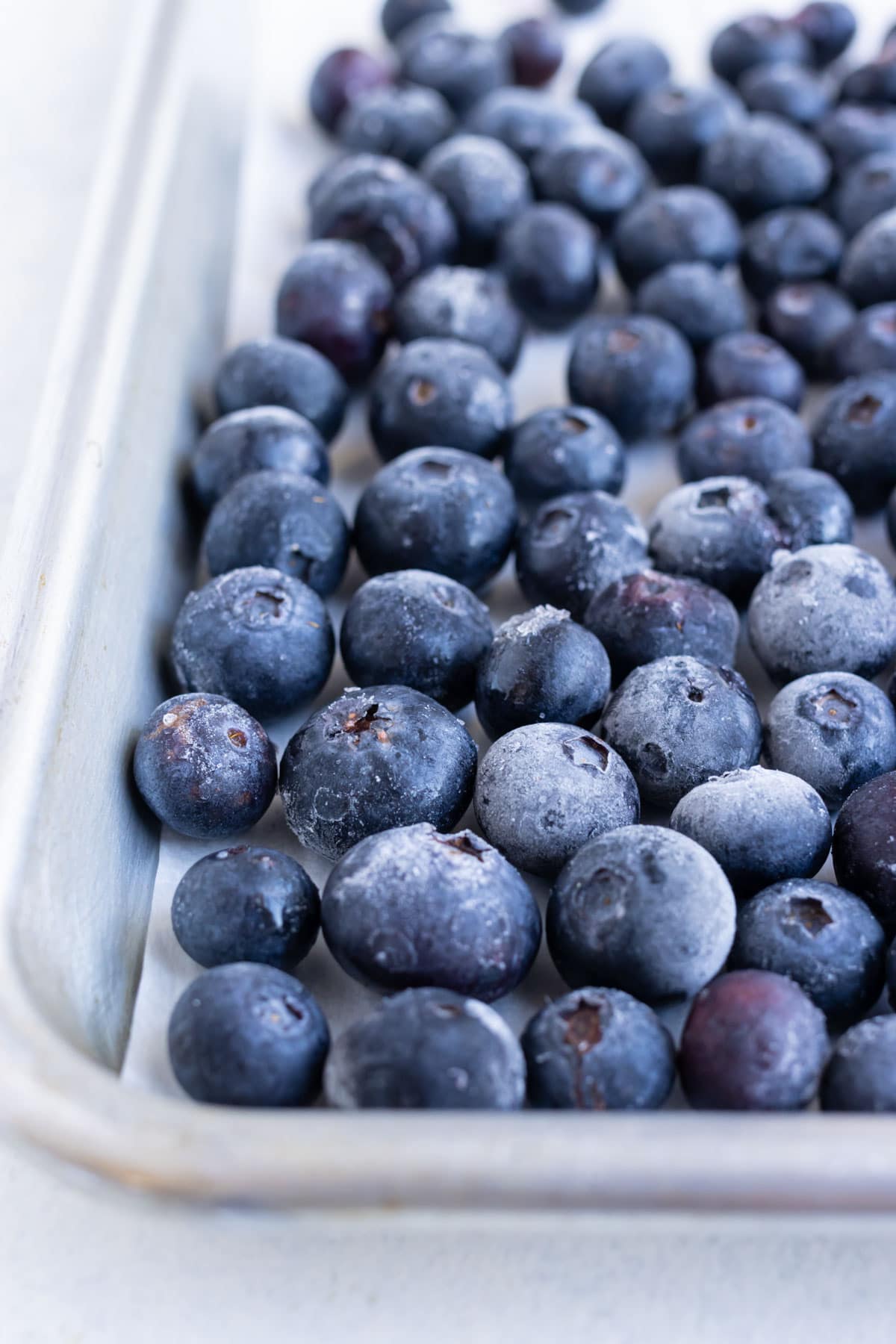 A baking sheet is covered with frozen blueberries.