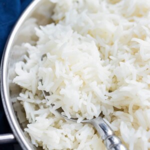 A closeup of cooked basmati rice being spooned out of a metal serving dish.