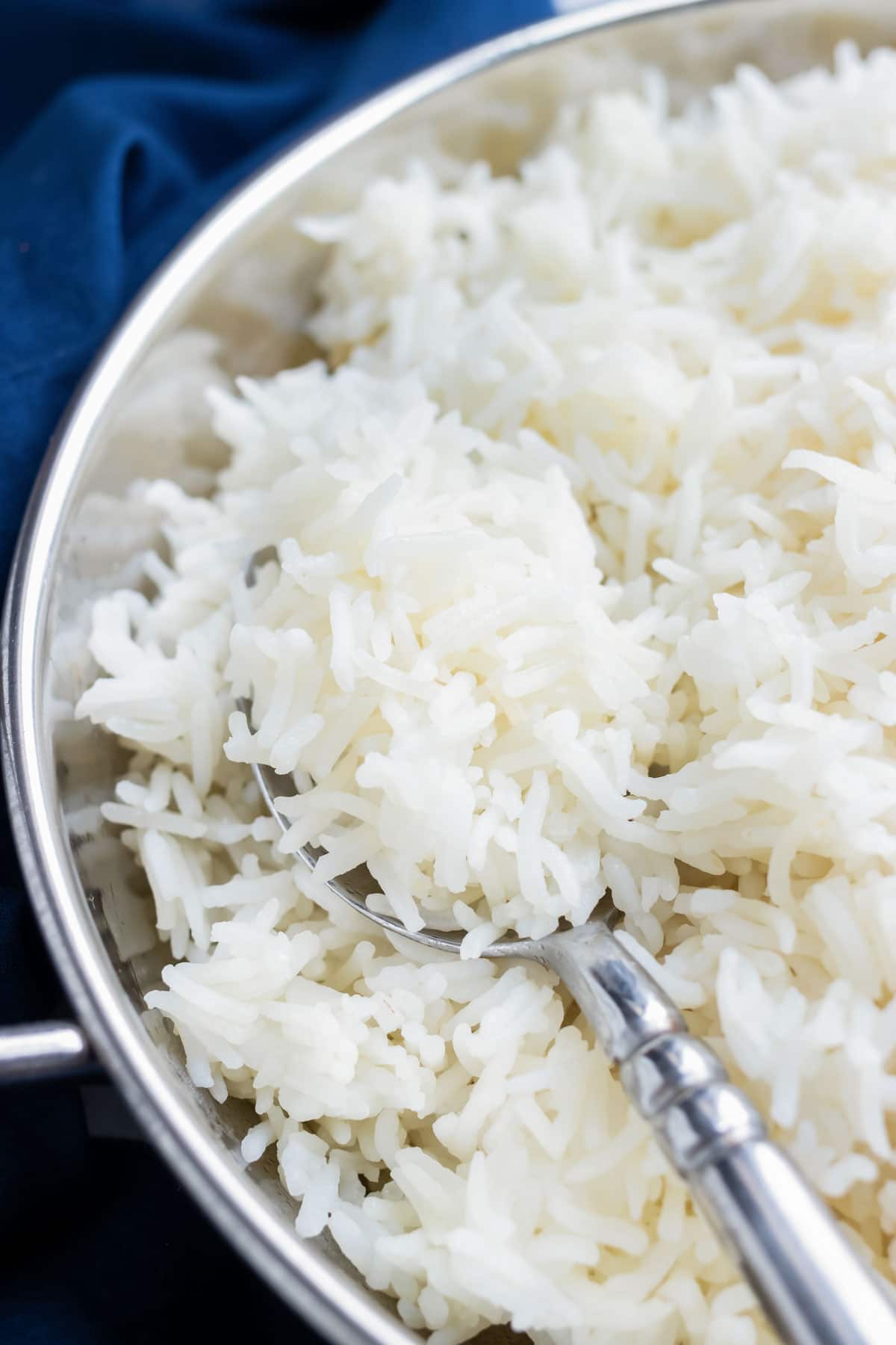 A closeup of cooked basmati rice being spooned out of a metal serving dish.