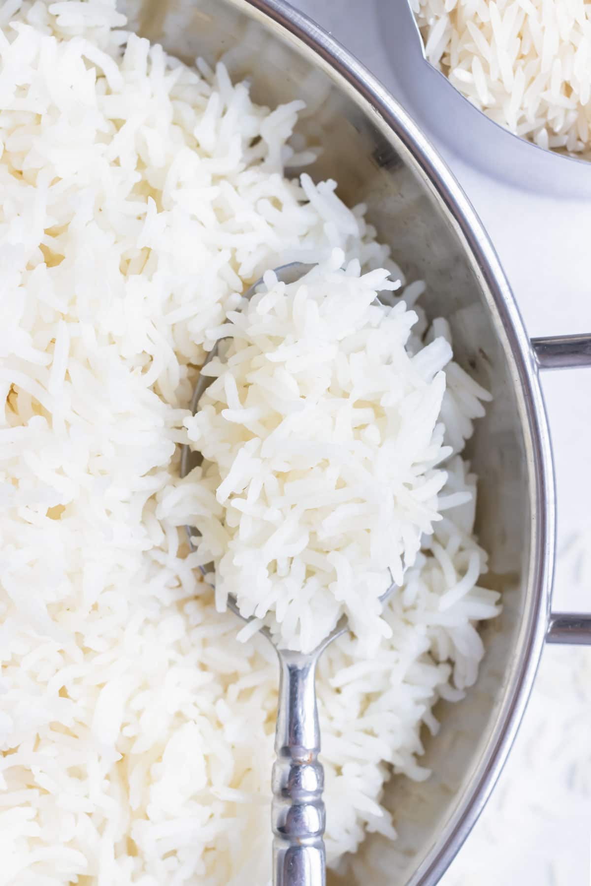 A closeup of cooked rice being spooned out of a metal serving dish.