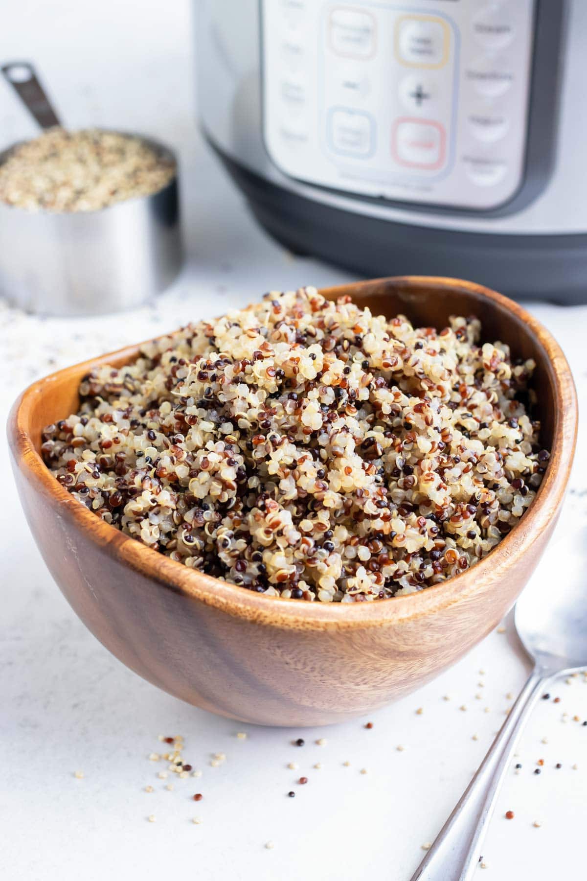 A wooden bowl full of cooked tri-color quinoa with an Instant Pot.