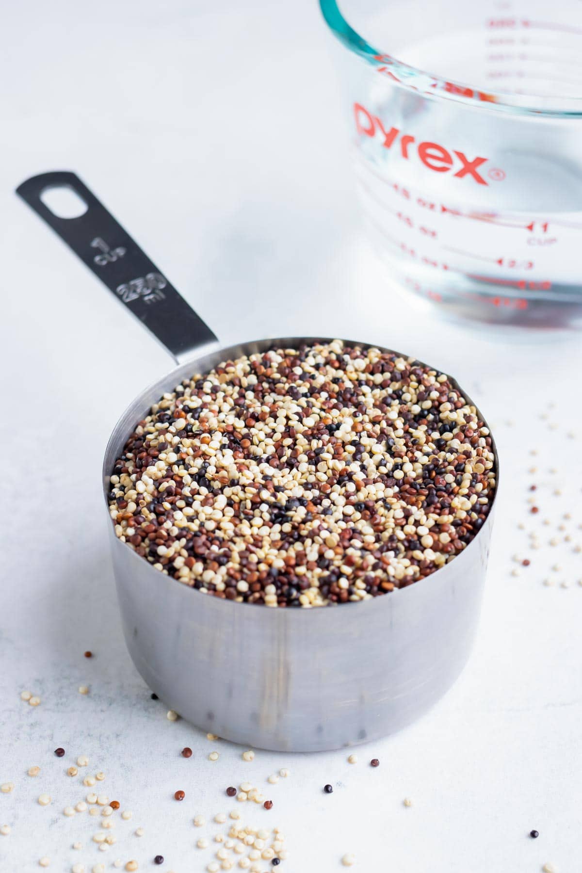 A 1 cup measuring cup that is full of red, white, and black dry quinoa to show the ratio with water.