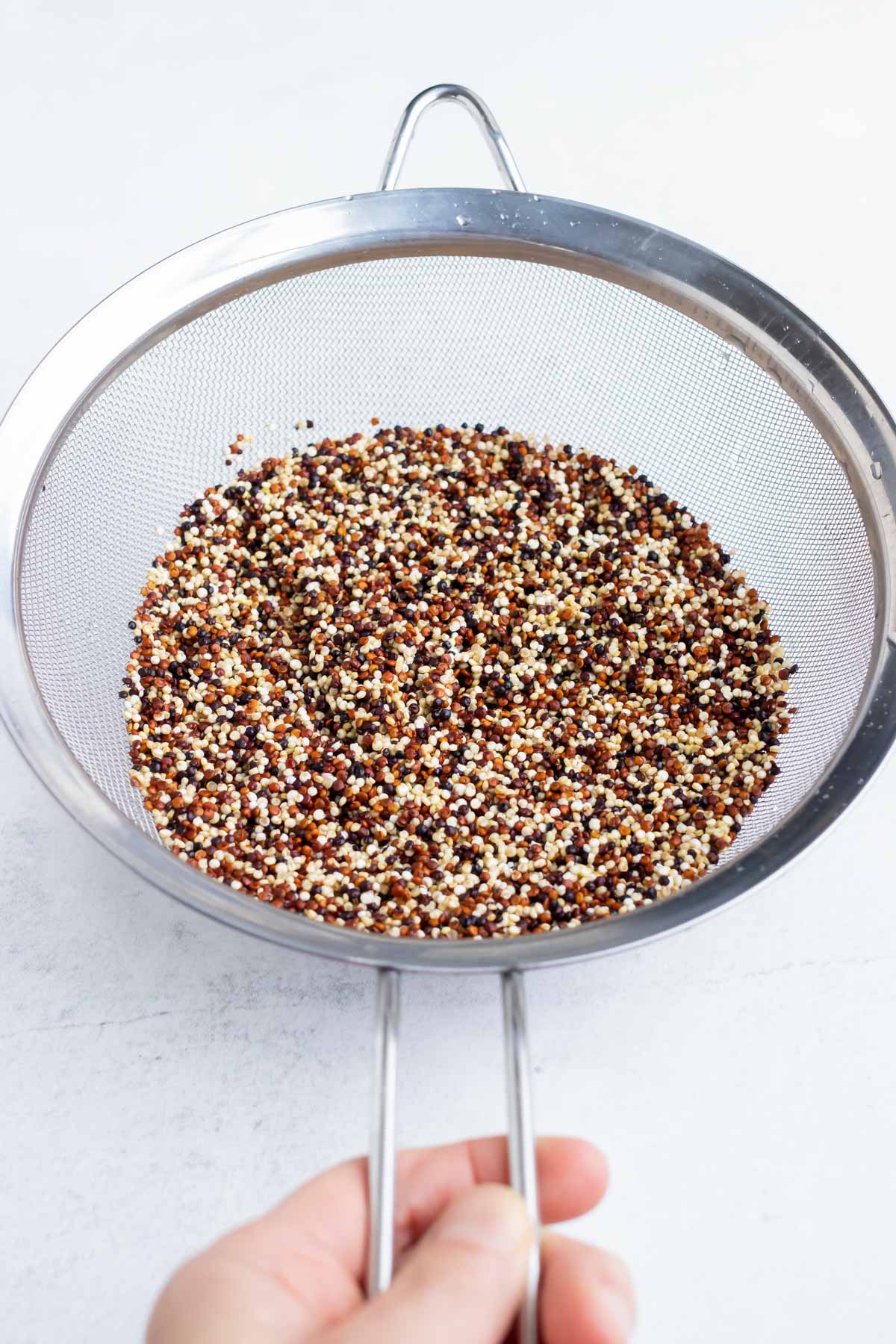 A fine mesh strainer with quinoa that has been rinsed with water.