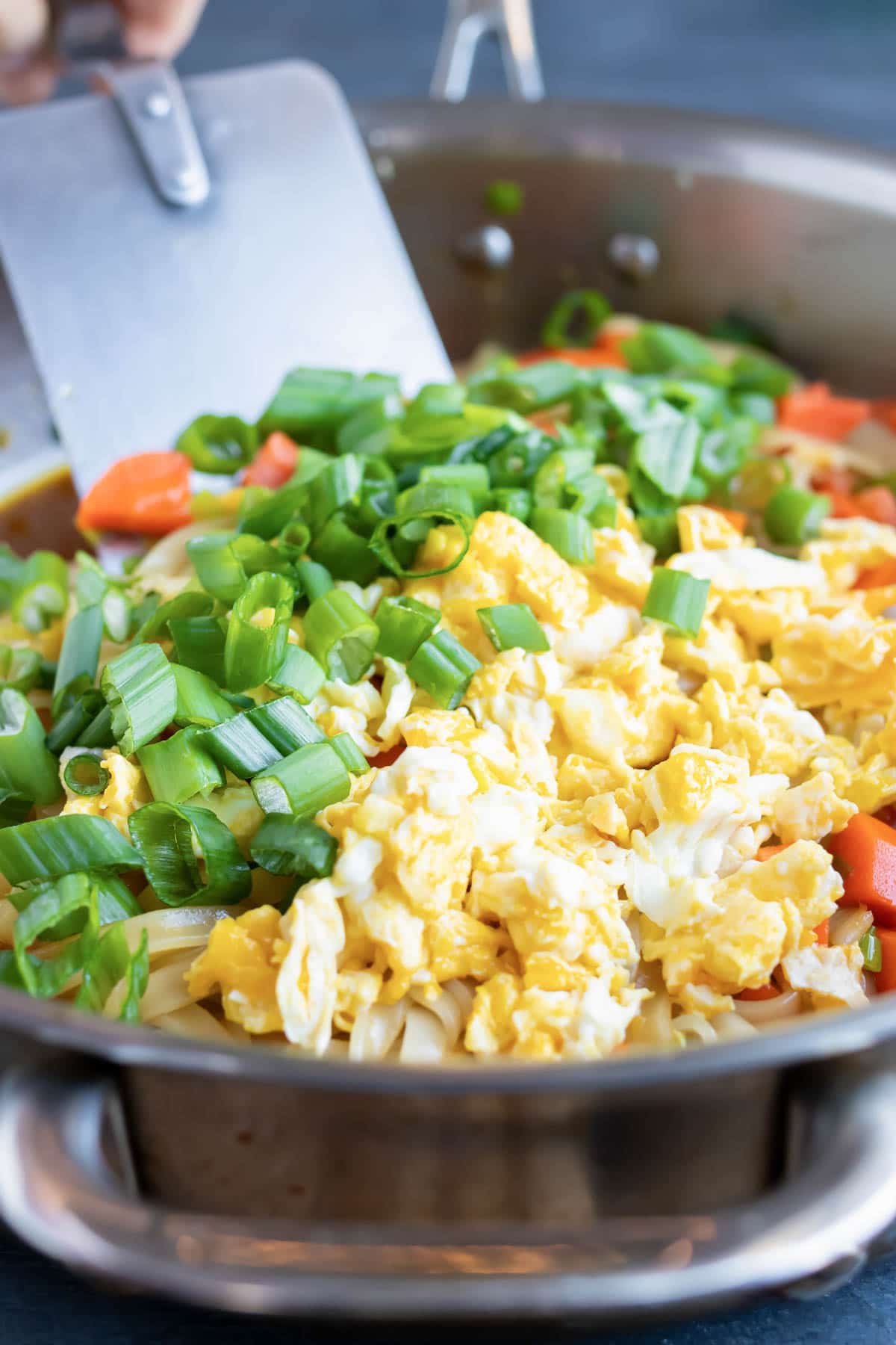 Combining eggs, green onions, and vegetables in a skillet for homemade pad Thai.