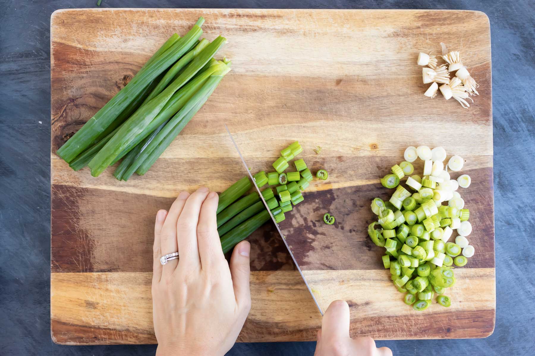 Using a knife to chop green onions For pad Thai on a cutting board.