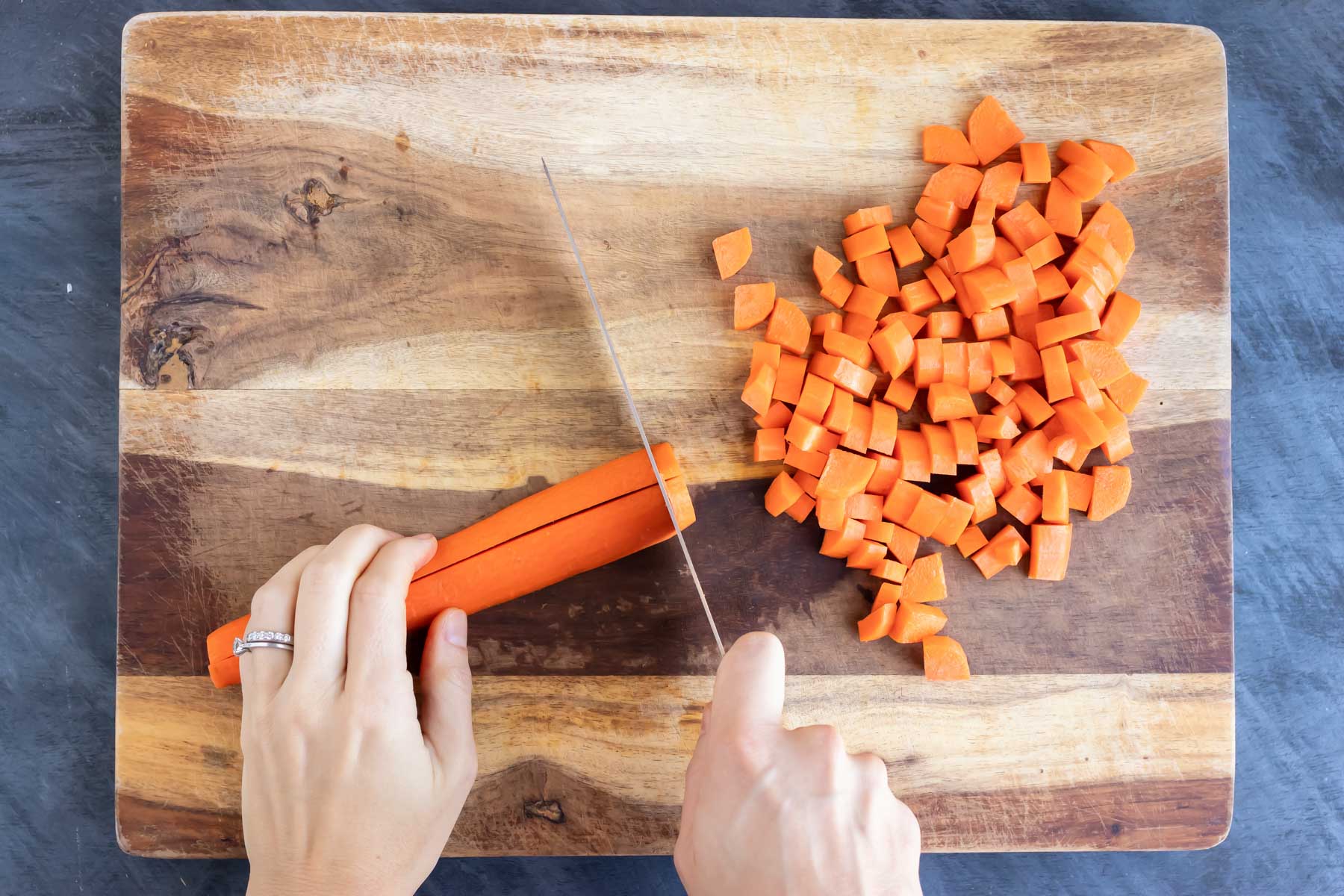 Using a knife to chop carrots for pad Thai on a cutting board.