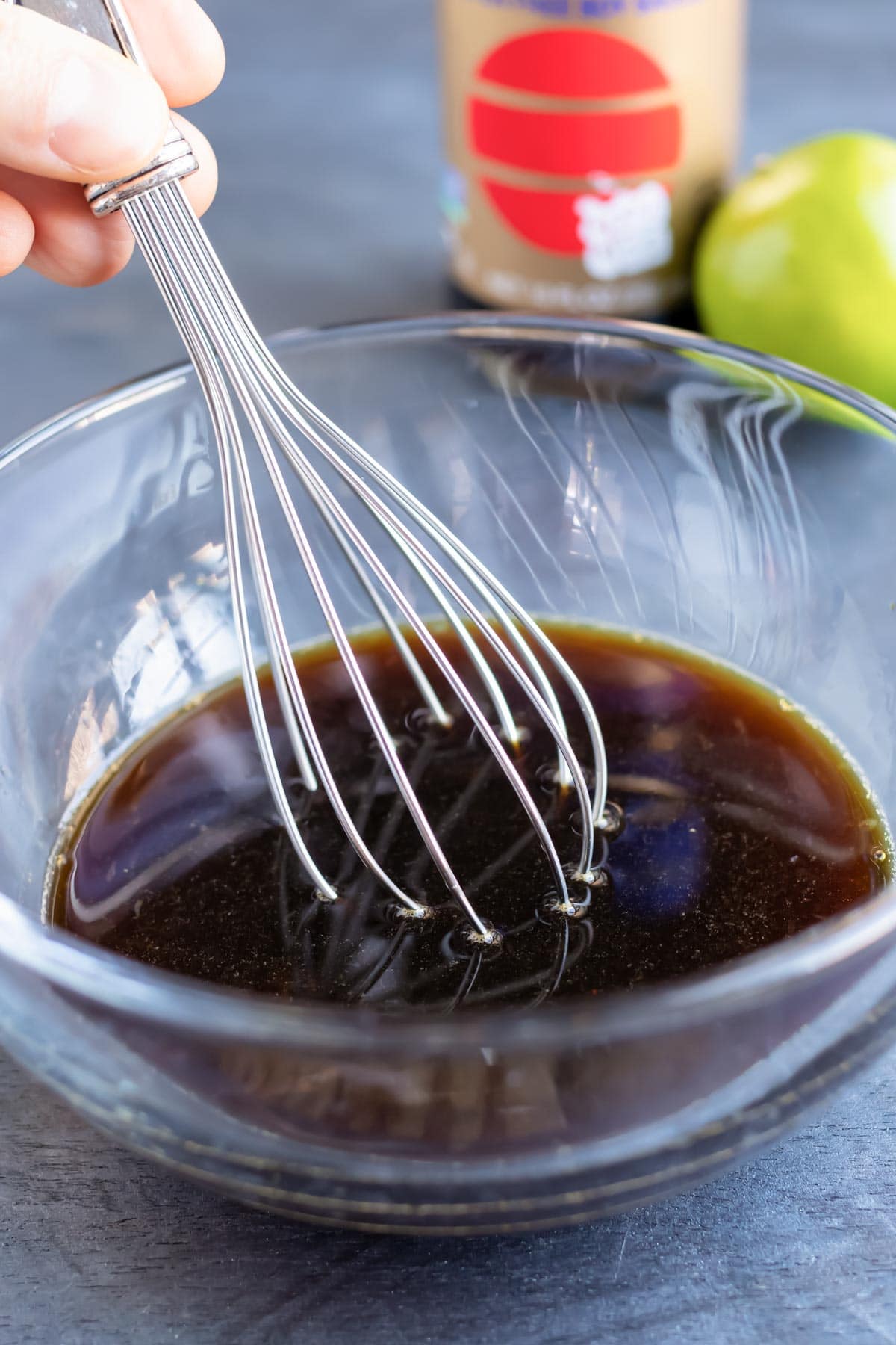 Pad Thai sauce being whisked together in a bowl with soy sauce and a lime in the background.