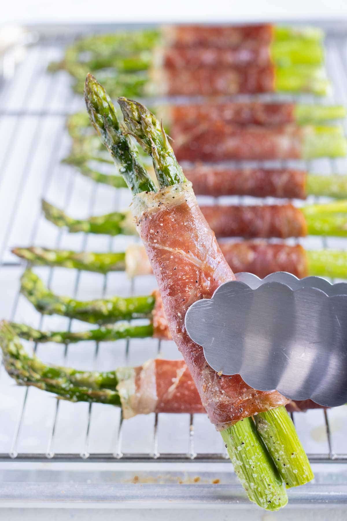 Tongs are shown holding the asparagus bundles from the baking sheet.
